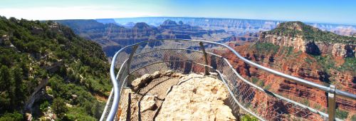 A panoramic view of the Grand Canyon from a lookout point, featuring rocky cliffs and vibrant red rock formations.