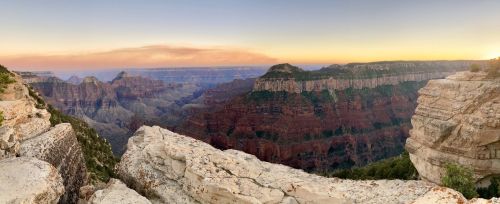 Panoramic view of the Grand Canyon at sunset, showcasing layered rock formations and distant cliffs.