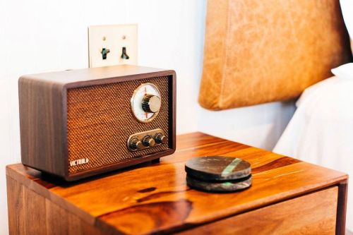 A vintage-style wooden radio sits on a bedside table next to a round stone coaster.