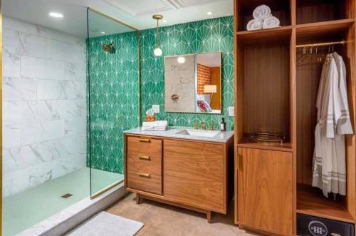 Modern bathroom featuring a glass shower, green geometric tile, wooden vanity, and neatly arranged towels.
