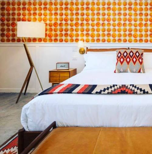 A stylish bedroom featuring a patterned wall, a cozy bed with decorative pillows, and a mid-century lamp.