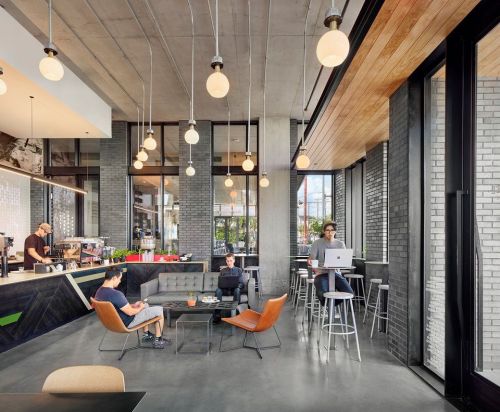A modern café interior with hanging lights, a barista, and patrons working at tables and on laptops.