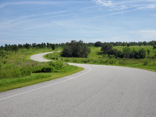 A winding road curves through a green landscape under a clear blue sky.