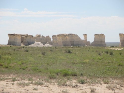 A vast landscape featuring unique rock formations against a clear blue sky, surrounded by green grass and sparse vegetation.
