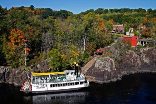 A scenic view of a riverboat docked near colorful autumn trees and a quaint riverside town.