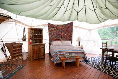 Cozy tent interior with a bed, wooden furniture, and colorful textiles, set in a natural, rustic environment.