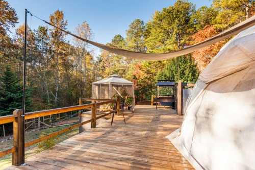 A wooden deck with a shade sail, surrounded by trees in autumn colors, featuring a gazebo and outdoor seating area.