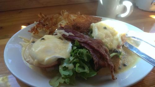 A plate of eggs Benedict with bacon, salad, and crispy hash browns, served with a cup in the background.