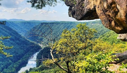Scenic view of a river winding through lush green mountains under a blue sky with scattered clouds.