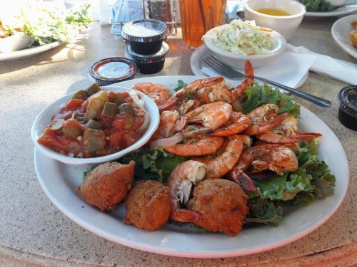 A plate of seasoned shrimp on lettuce, served with a side of vegetable stew and two hushpuppies.