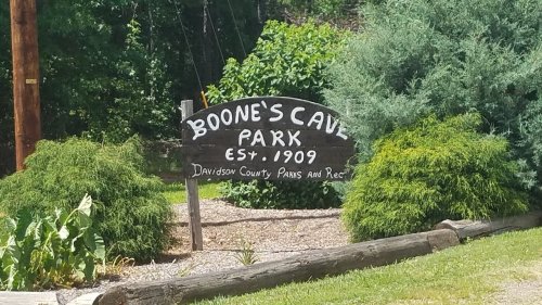Sign for Boone's Cave Park, established in 1909, surrounded by greenery and trees.