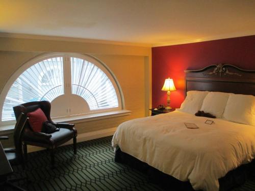 Cozy hotel room featuring a large window, a king-sized bed, a desk, and a lamp, with a patterned green carpet.