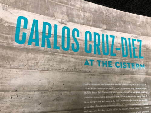 Text on a concrete wall reads: "Carlos Cruz-Diez at the Cistern" with a description of the artist's work.