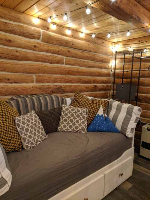 Cozy log cabin interior with a sofa adorned with various patterned pillows and warm string lights overhead.