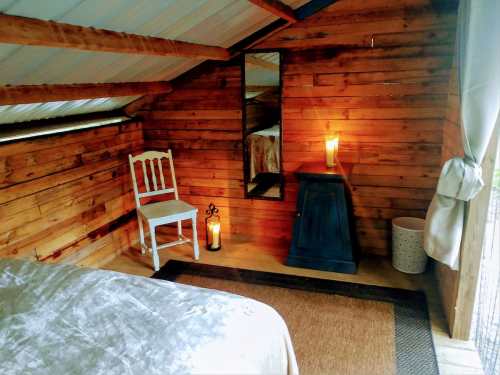 Cozy wooden interior with a bed, chair, mirror, and candles, creating a warm, inviting atmosphere.