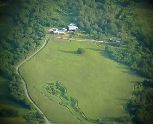 Aerial view of a green landscape with a winding road and several buildings surrounded by trees.