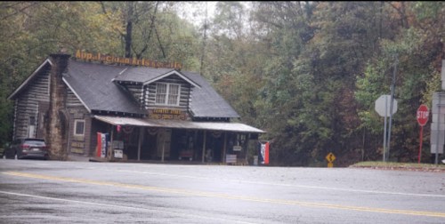 A rustic wooden building labeled "Appalachian Arts & Crafts" beside a road, surrounded by trees in a rainy setting.