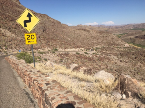 Curvy road sign with a speed limit of 20 MPH, surrounded by rocky terrain and clear blue skies.