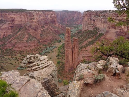 A stunning view of red rock formations and a canyon, with two towering spires rising above a lush green valley.