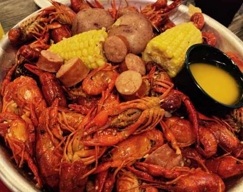 A platter of crawfish, potatoes, corn, and sausage, served with a small bowl of dipping sauce.