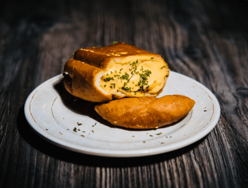 A toasted sandwich filled with creamy cheese and herbs, served on a white plate with a rustic wooden background.