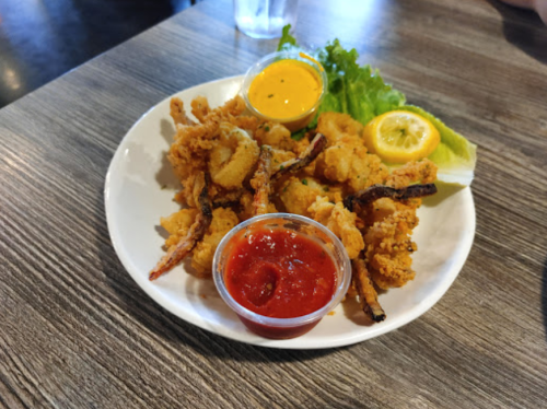 A plate of fried seafood with dipping sauces, lettuce, and lemon on a wooden table.