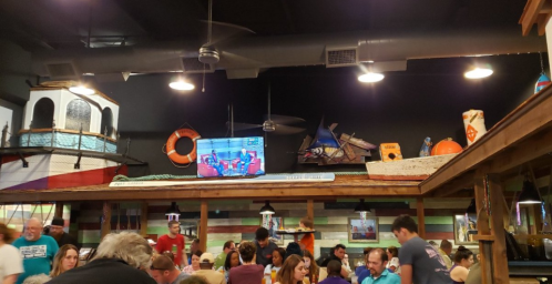 A lively restaurant interior with a crowd, colorful decor, and a TV displaying a show in the background.