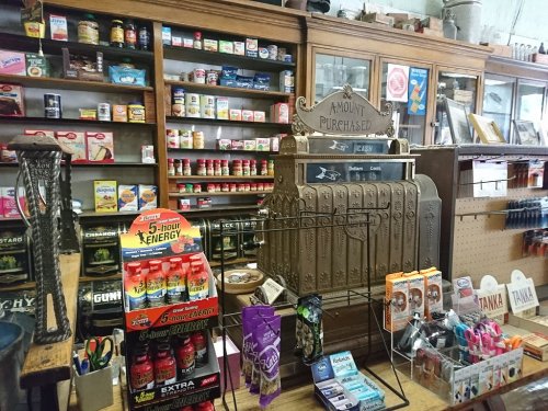 A vintage store interior featuring an old cash register, shelves of goods, and various products on display.
