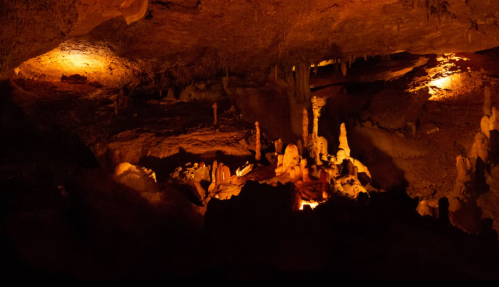 A dimly lit cave interior featuring stalactites and stalagmites illuminated by warm orange lights.