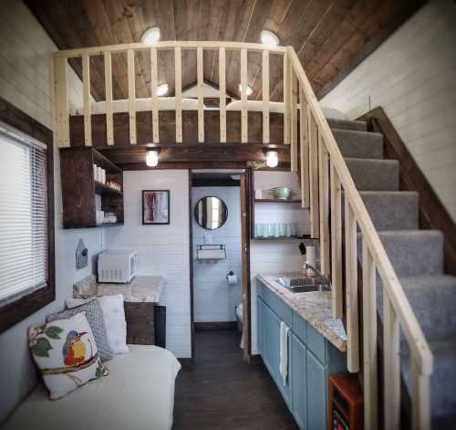 Cozy tiny house interior featuring a loft, kitchen area, and living space with wooden accents and modern decor.