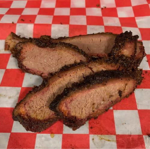 Sliced smoked brisket on a red and white checkered paper, showcasing a smoky crust and tender interior.