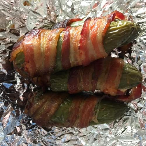 Bacon-wrapped jalapeños resting on aluminum foil, showcasing a crispy, golden-brown exterior.
