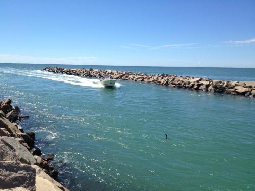 A boat navigates a narrow waterway lined with rocky jetties under a clear blue sky.