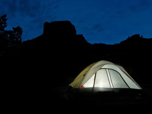 A lit tent stands against a dark mountain silhouette under a night sky.