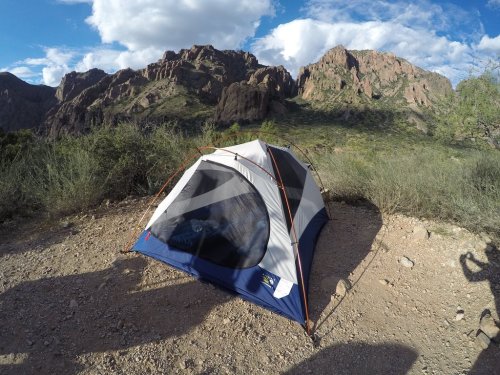 A tent set up on rocky ground with mountains and blue skies in the background.