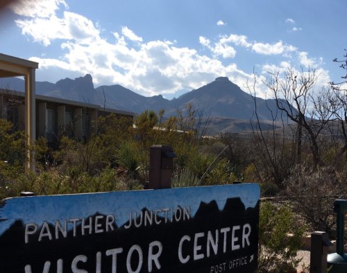 A sign for Panther Junction Visitor Center with mountains and a blue sky in the background.