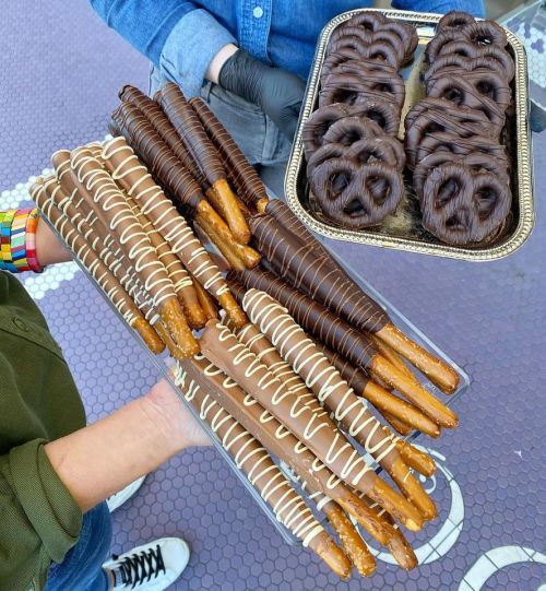 A tray of chocolate-covered pretzel sticks and chocolate-dipped pretzels held by two people.