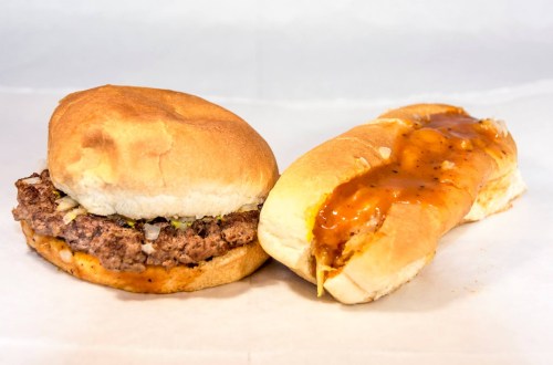 A hamburger with lettuce and a hot dog topped with sauce, both on soft buns, placed on a white surface.
