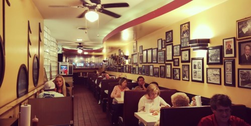 A cozy diner interior with booths, patrons dining, and walls adorned with framed photos and memorabilia.