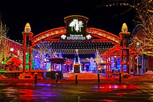 A festive entrance to The Shops at Riverwoods, adorned with colorful lights and decorations at night.