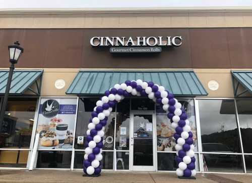 Exterior of Cinnaholic store with a purple and white balloon arch at the entrance.