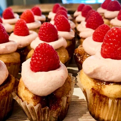 A close-up of cupcakes topped with pink frosting and fresh raspberries, arranged neatly on a tray.
