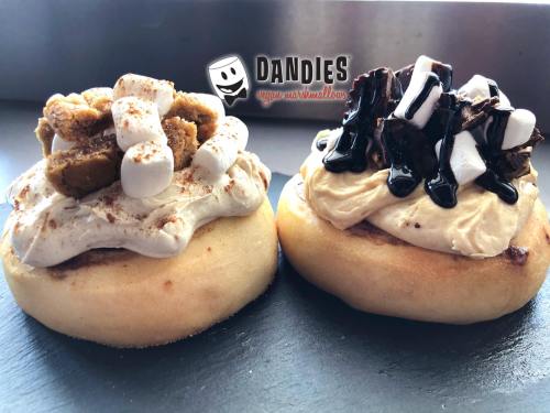 Two dessert donuts topped with marshmallow cream, crushed cookies, and chocolate drizzle, one with mini marshmallows.