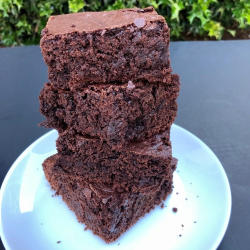 A stack of four rich, fudgy chocolate brownies on a white plate against a green background.