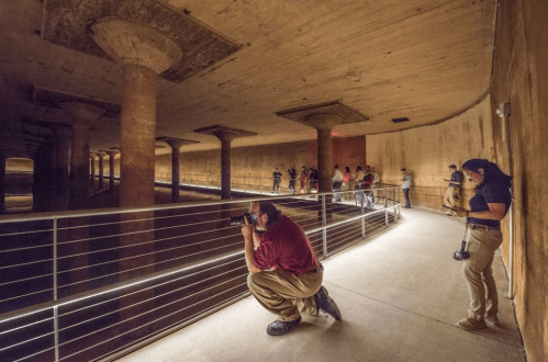 A dimly lit underground space with pillars, where people are exploring and taking photos along a railing.