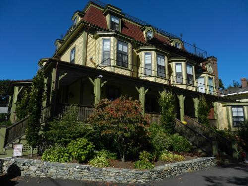 A large, yellow Victorian-style house with multiple gabled roofs and a landscaped front yard under a clear blue sky.