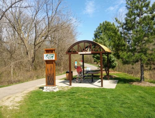 A bike resting at a shelter along a trail, with a sign for "Auburn Hills" and trees in the background.
