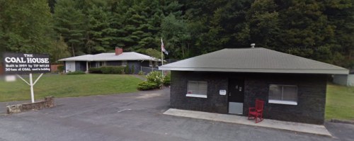 A small black building with a red chair outside, next to a larger house and a sign reading "The Coal House."