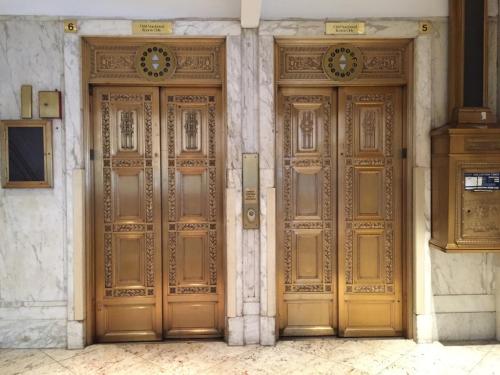 Two ornate gold elevators with decorative doors in a marble lobby, featuring a vintage elevator panel on the side.