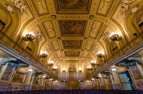 Opulent ballroom with ornate ceilings, chandeliers, and intricate wall designs, illuminated softly.